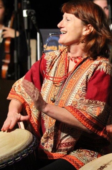 Annie Fletcher smiling while playing a djembe on stage